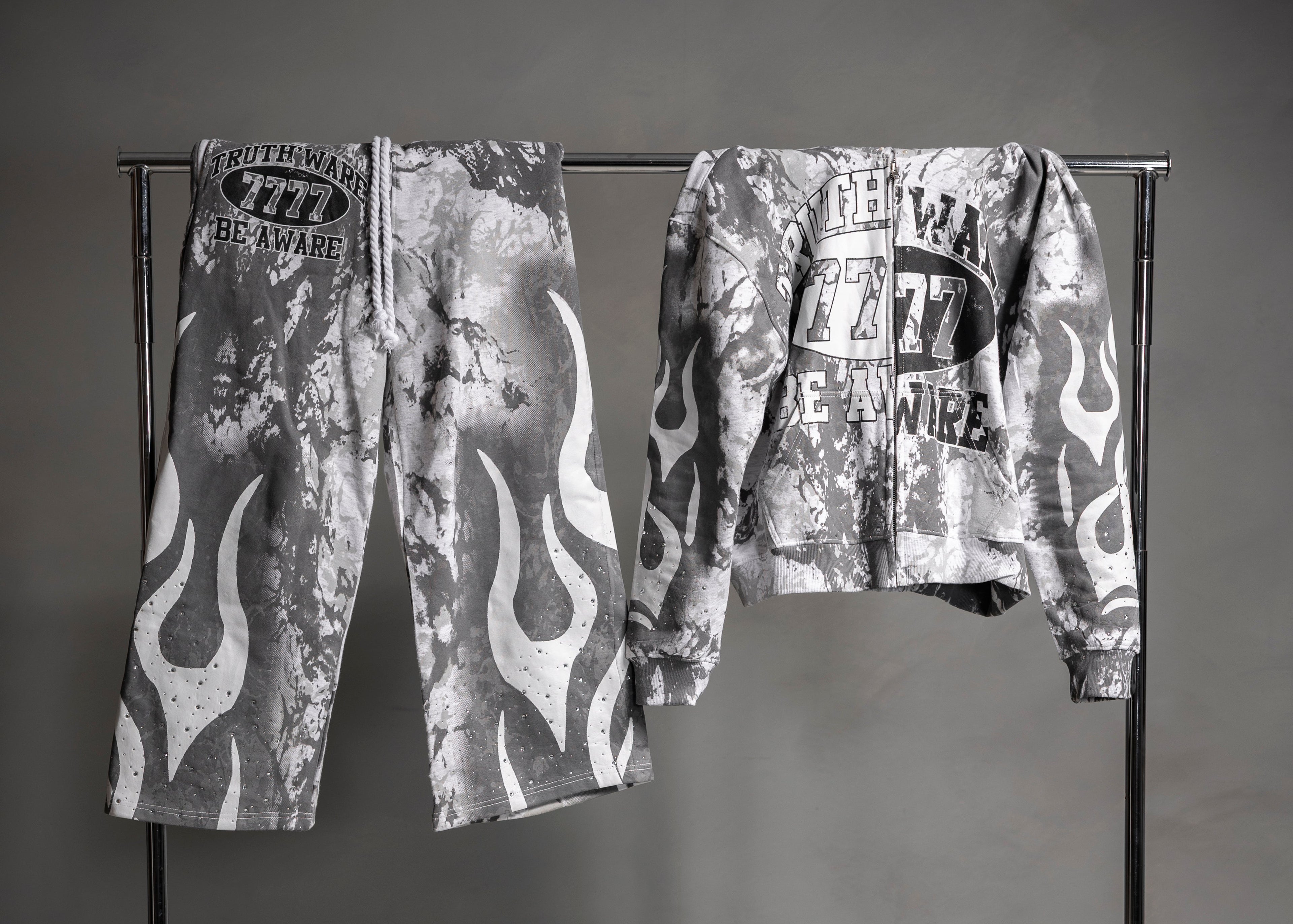 A black and white graphic clothing rack displaying a matching set: flame-patterned pants on the left and a matching graphic sweatshirt on the right, set against a dark gray studio background.